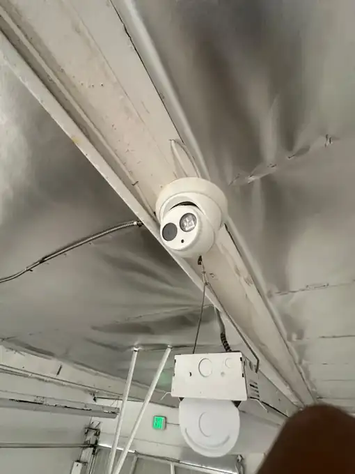 Ceiling-mounted turret security camera installed on an exposed structural beam, with cable routed along the beam