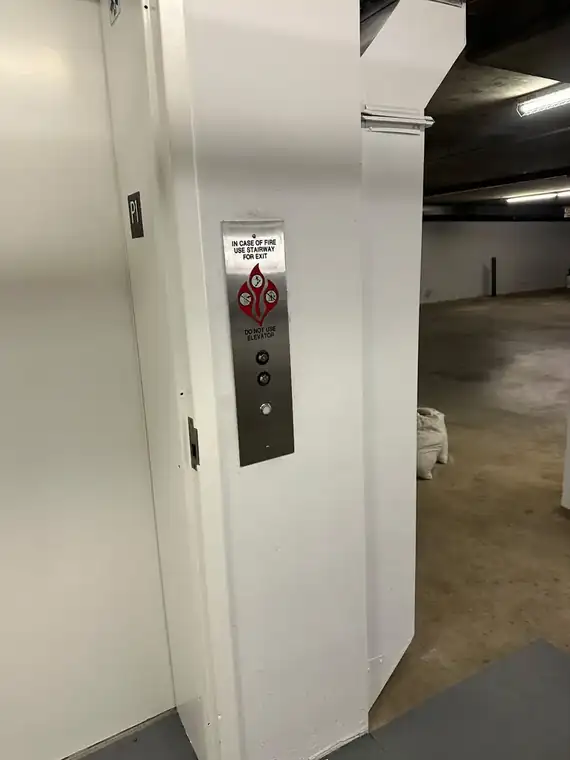 Elevator lobby on a parking level with the stainless hall-call panel mounted beside the elevator door