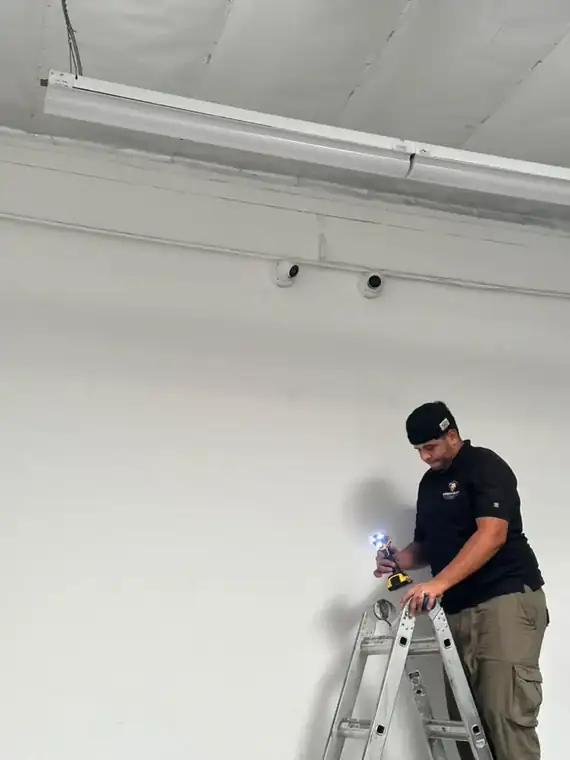 Defender Solution technician on a ladder installing turret security cameras along a ceiling beam